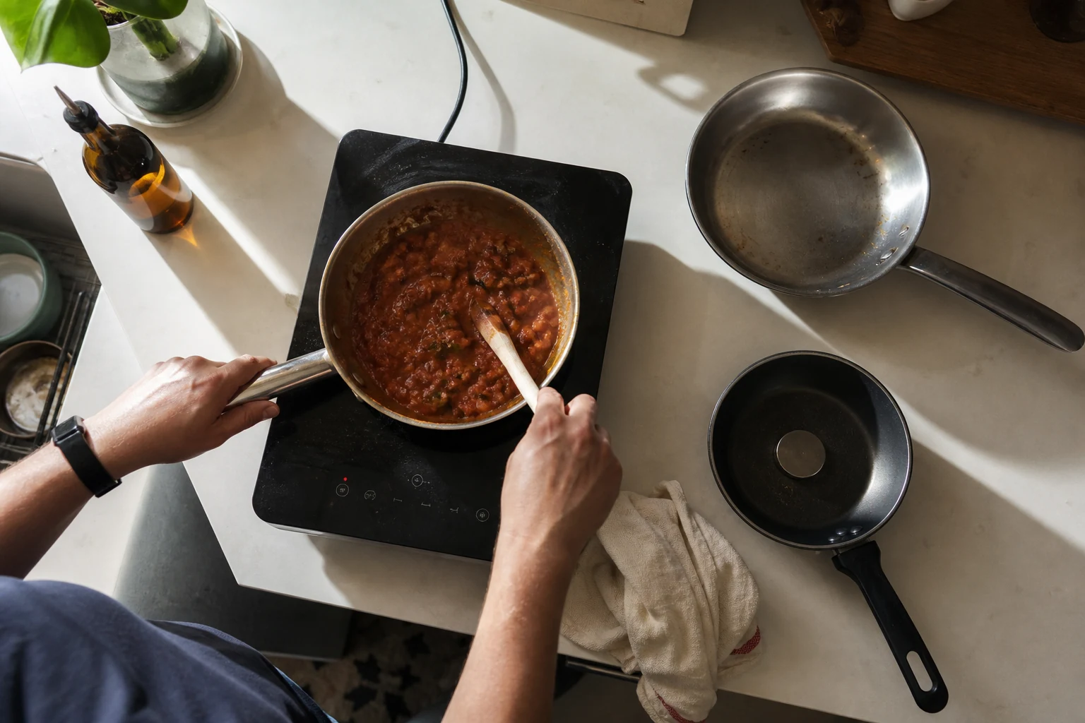 Hands cooking tomato sauce on a portable induction burner